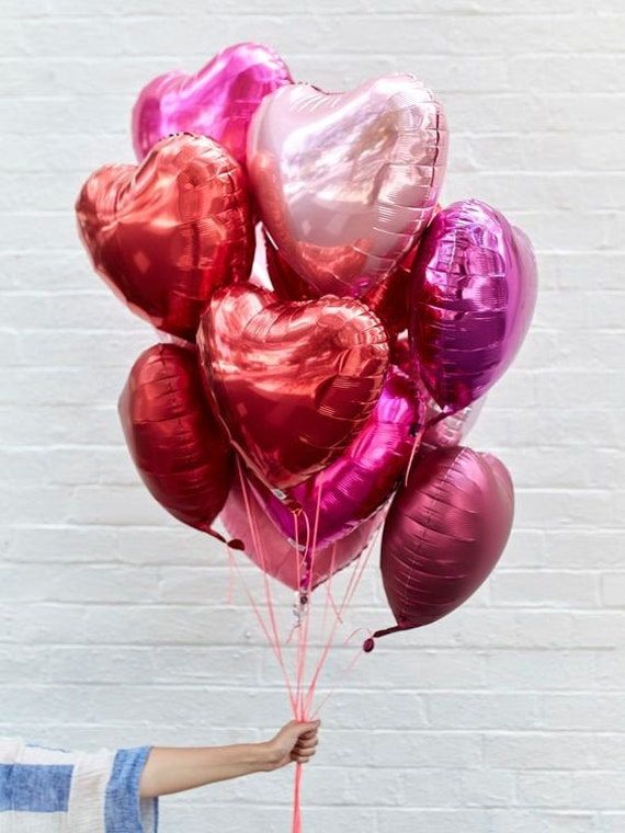 En hand som håller i ett stort knippe hjärtformade folieballonger fyllda med helium.