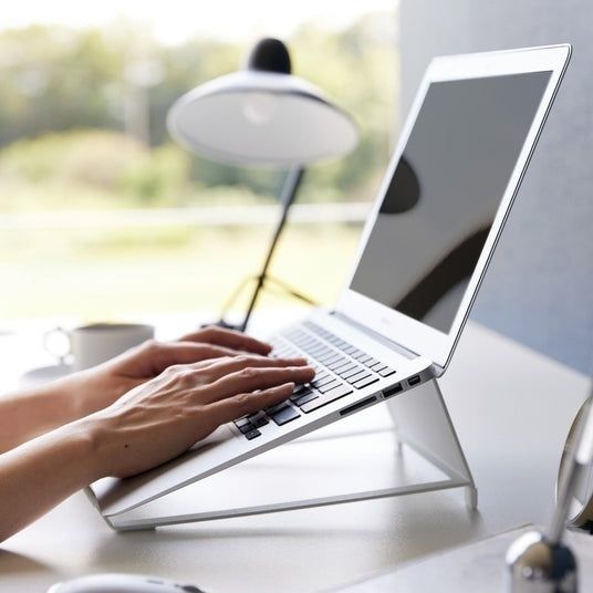 Händer skriver på en laptop placerad på ett höjande laptopstativ